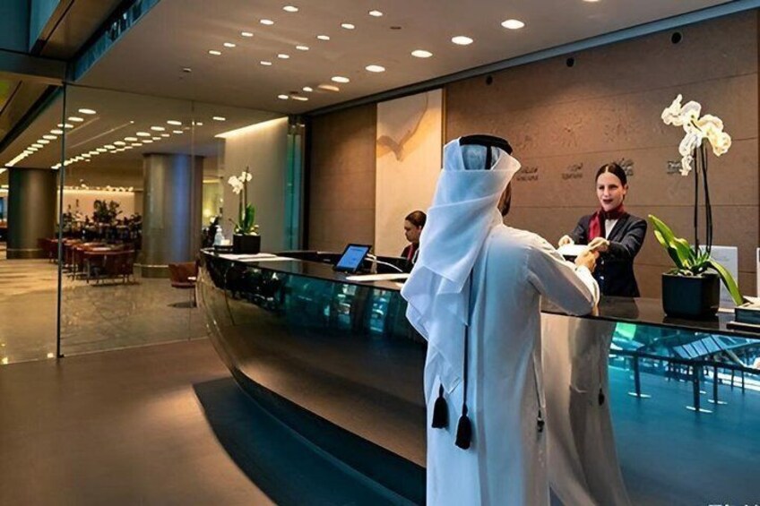 A modern hotel lobby with a reception desk, a receptionist, and a guest in traditional attire. 1