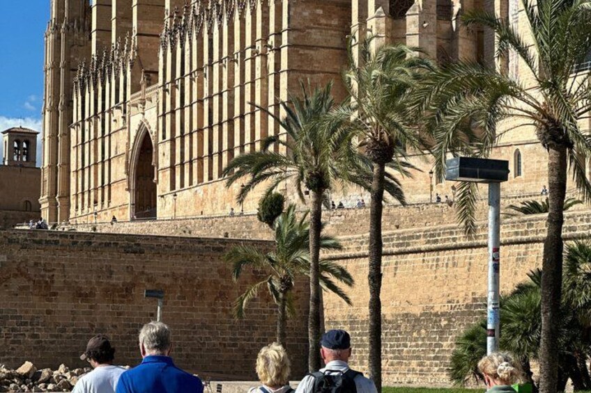 A historic building with a large arched entrance, palm trees, and a stone wall. 5