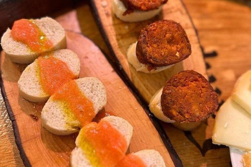 Sliced bread with a red topping and a round, brown item on a wooden board. 2