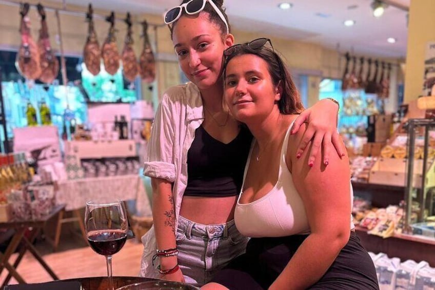 Two people sitting at a table with a wine glass, in a store with hanging items in the background. 5