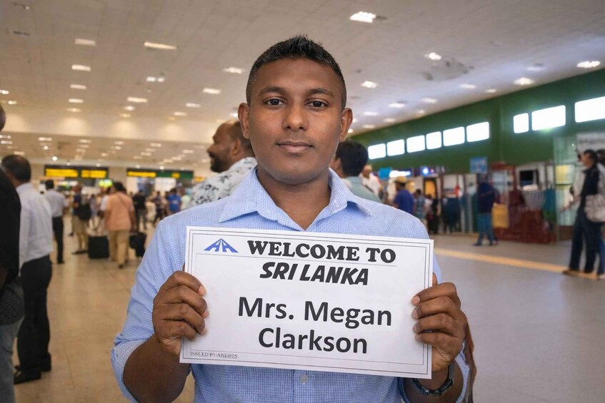 A person holding a sign that reads 'WELCOME TO SRI LANKA Mrs. Megan Clarkson' in a busy indoor setting. 2