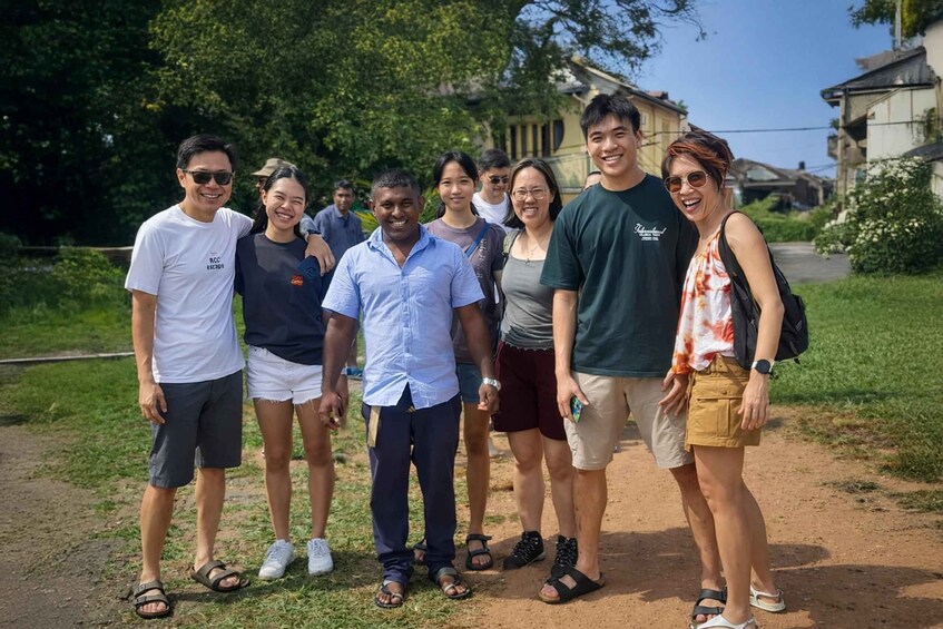 A group of people standing on a dirt path with greenery and buildings in the background. 5