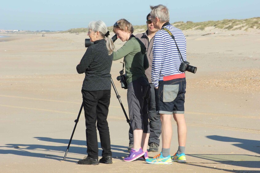 Four people on a sandy beach with a camera and tripod. 2