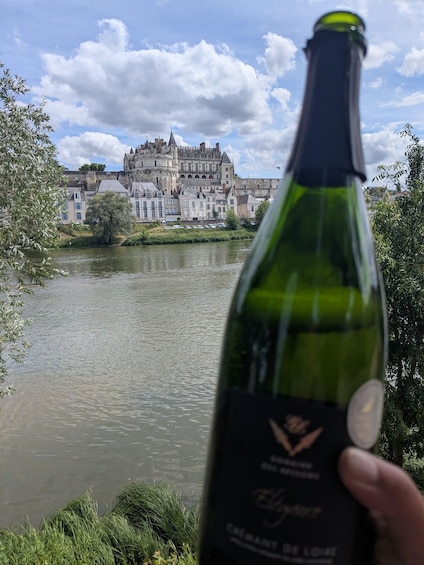 A bottle of wine with a label, held in front of a river with a historic building in the background. 2