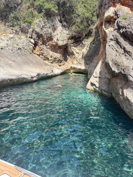 A clear blue pool surrounded by rocky cliffs and sparse vegetation. 2