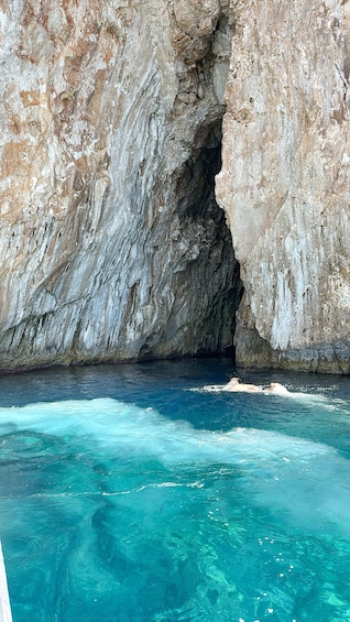 A rocky cliff with a cave entrance and clear turquoise water. 5
