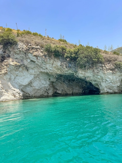 A coastal cliff with a cave entrance and clear turquoise water. 4