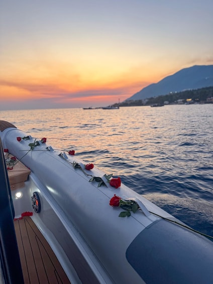 A boat deck decorated with red roses, a wooden floor, and a sunset over the water. 3