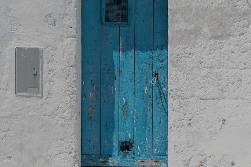 Una puerta azul desgastada con pintura descascarada en una pared blanca. 3