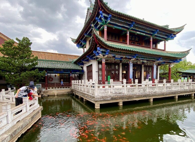 A traditional Chinese pavilion over a koi pond with people on the bridge. 3