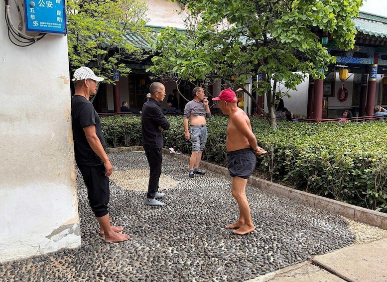 Four men standing on a pebbled area with a traditional building in the background. 2