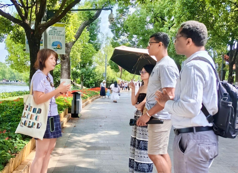 A group of people standing on a tree-lined path with a body of water in the background. 1