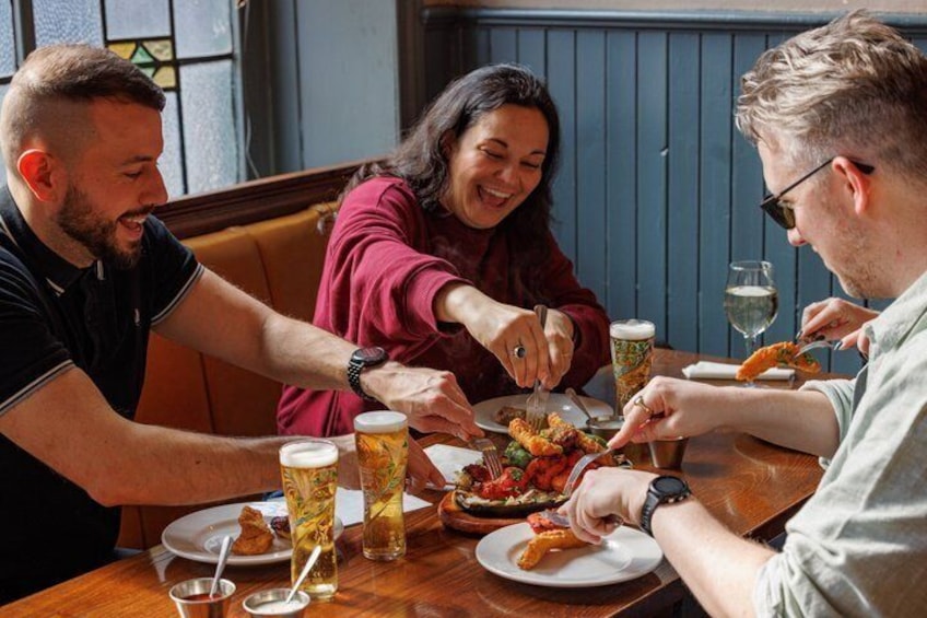 A group of people dining at a restaurant with a wooden table, plates of food, and beer glasses. 1