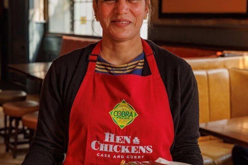 A person wearing a red apron with 'Cobra' and 'Hen & Chicks' logos, indicating a restaurant setting. 5