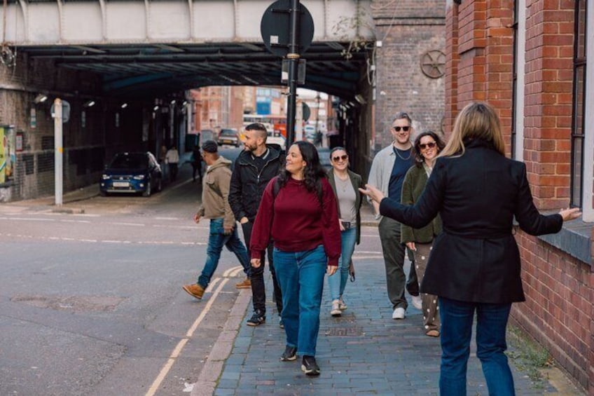 A group of people walking on a city street with a brick building and a covered passageway in the background. 3