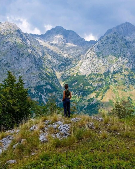 A person standing on a grassy hill overlooking a mountainous landscape. 4