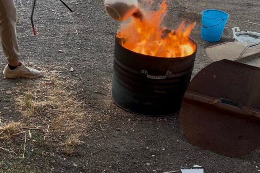A person pouring a liquid into a barrel that is on fire. 5