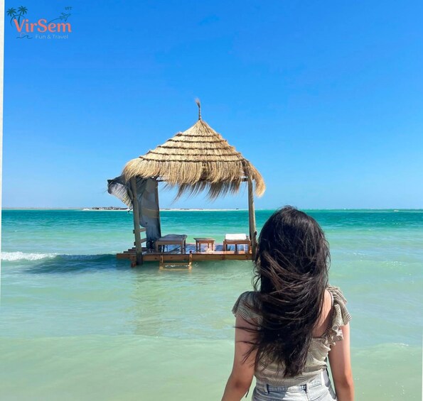 A beach with a thatched-roof structure and lounge chairs. 5