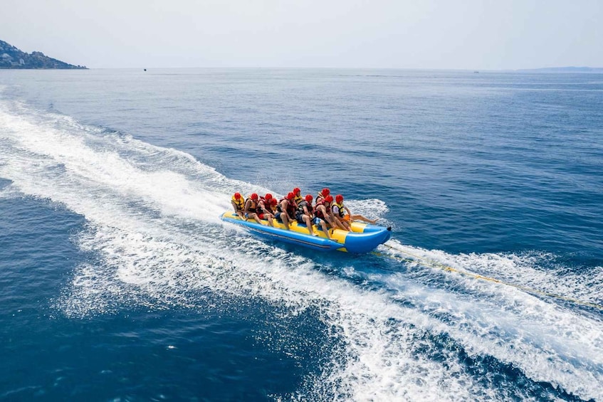 A group of people in a blue raft with red helmets, being towed by a boat on a calm sea. 2