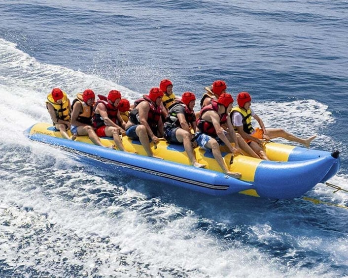A group of people in a blue and yellow raft, wearing red helmets, paddling on the water. 1