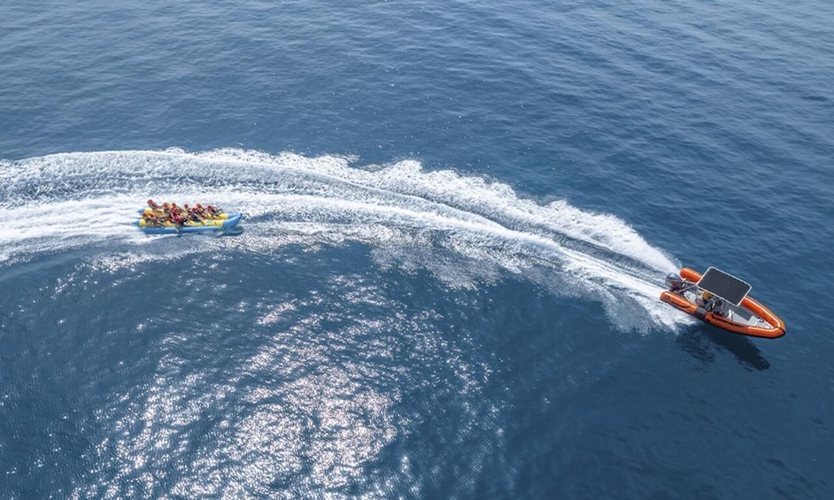 A blue raft with people and an orange speedboat creating a wake in the ocean. 3