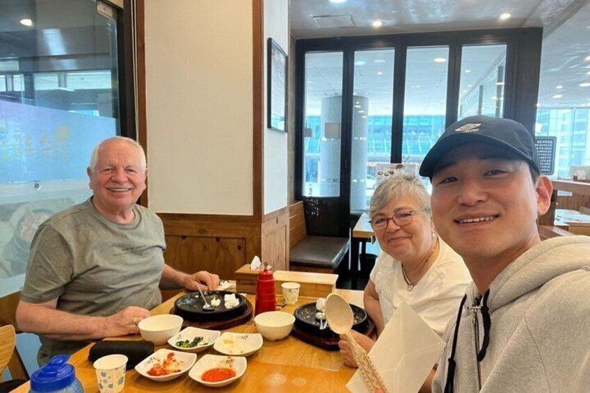 Three people seated at a table with food and condiments in a restaurant with large windows. 3