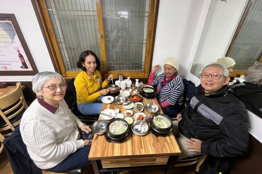 A group of people sitting around a wooden table with various dishes and bowls. 4