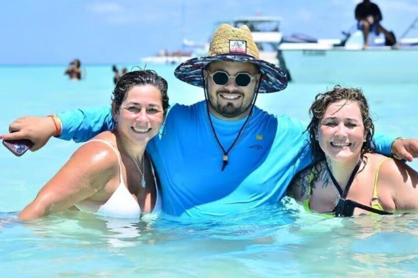 Three people in a clear blue sea with a boat in the background. 2