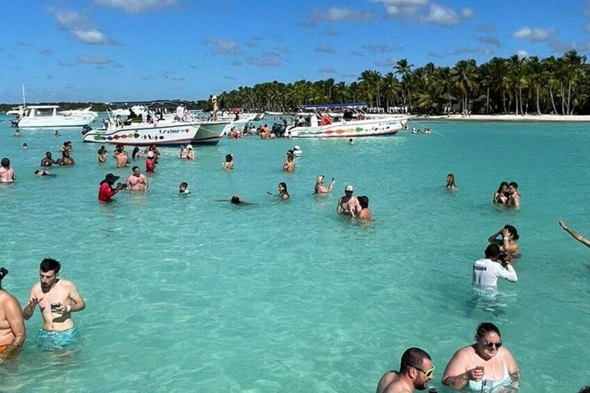 A crowded beach with people swimming and boats in the water. 2