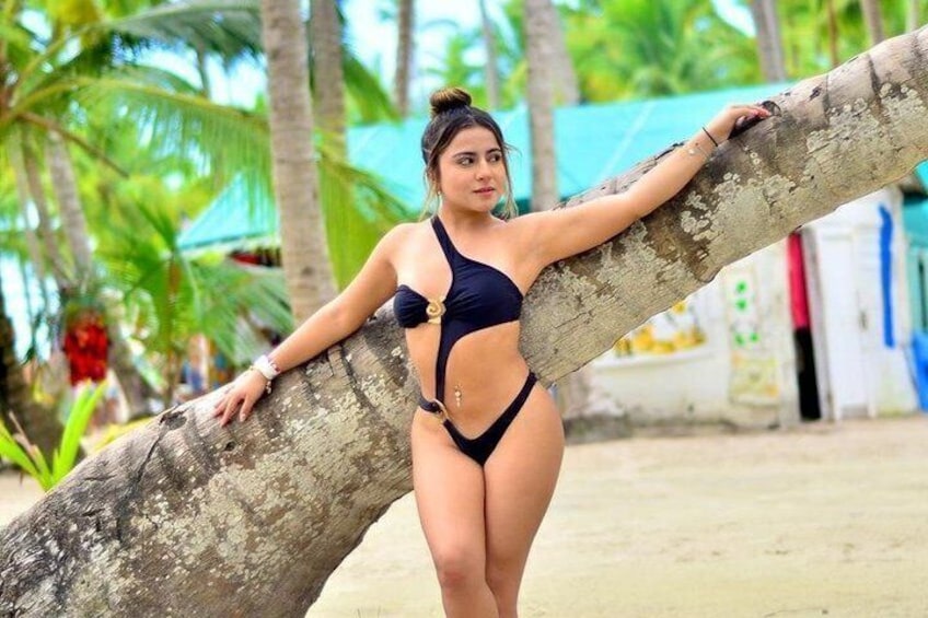 A person in a swimsuit leaning on a tree in a tropical setting. 1