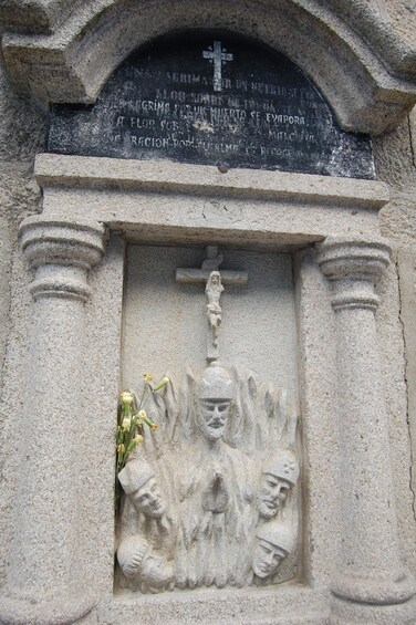 A stone monument with a cross and inscriptions, featuring a relief sculpture of a figure holding a child. 5
