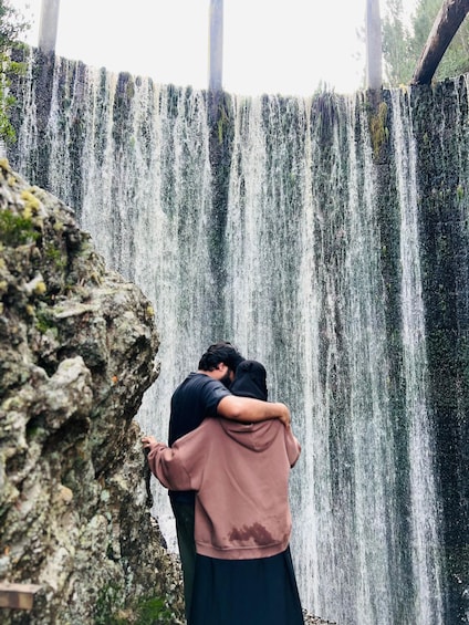 A waterfall with two people embracing in front of it. 2