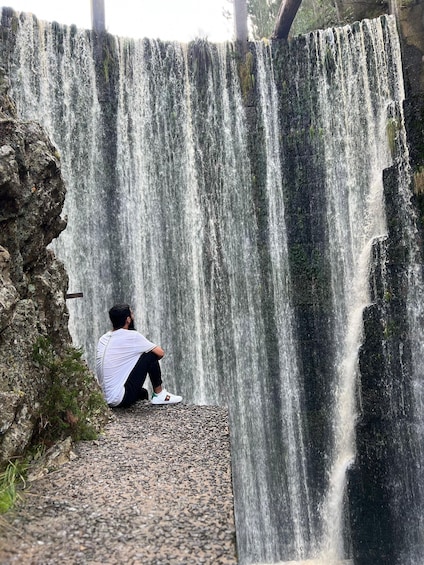 A person sitting on a stone ledge facing a waterfall. 3