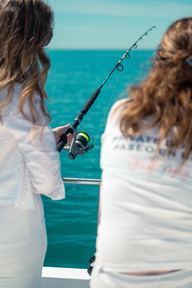 Two people fishing on a boat with a clear view of the ocean. 4