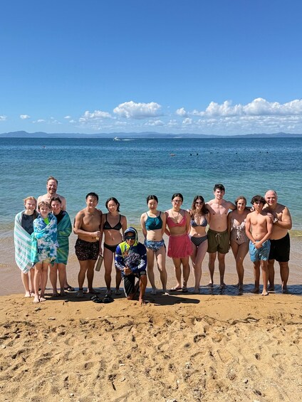 A group of people standing on a sandy beach with a clear blue sky and calm sea in the background. 3