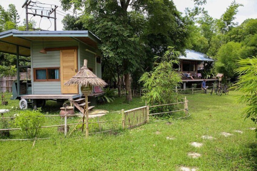 A small house with a thatched roof, a wooden deck, and a bicycle in a lush green garden. 3