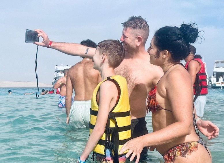 A group of people in shallow water, some wearing life jackets, with a boat in the background. 5
