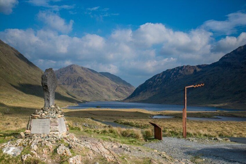 A stone monument, a body of water, and mountains in the background. 4