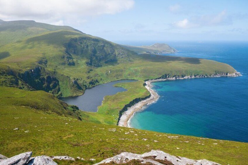 A coastal landscape with a bay, grassy hills, and a clear sky. 1