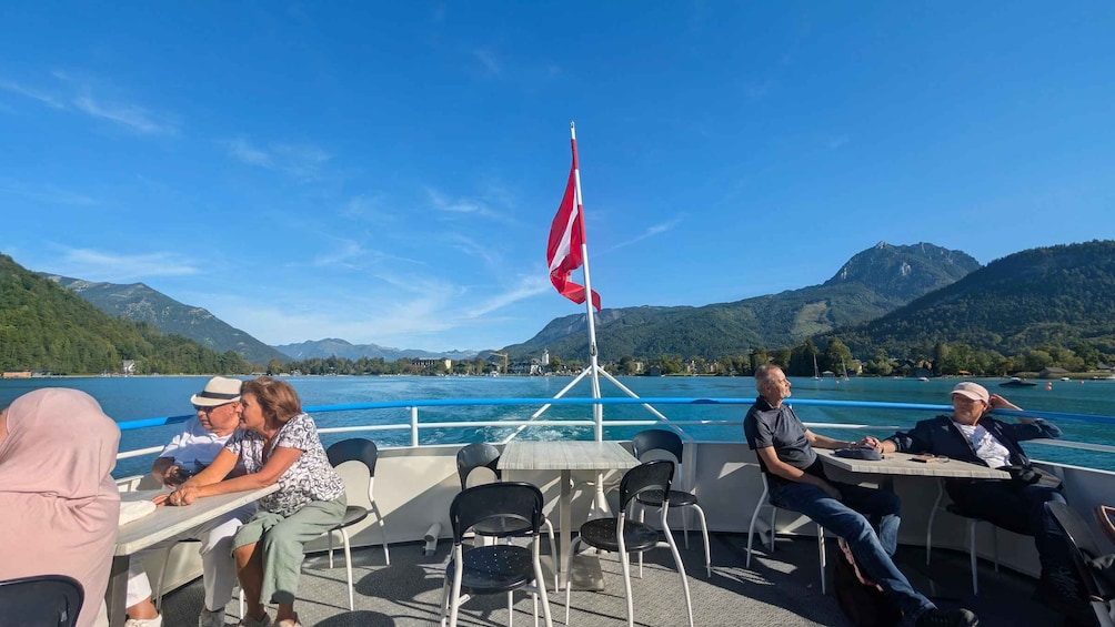 A group of people on a boat with a flag, surrounded by a mountainous landscape and a body of water. 4