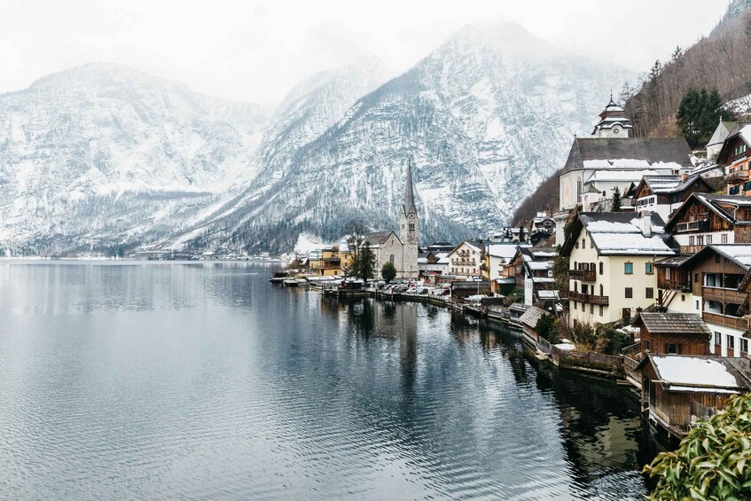 A snow-covered lake with buildings and a church along the shore, surrounded by mountains. 2