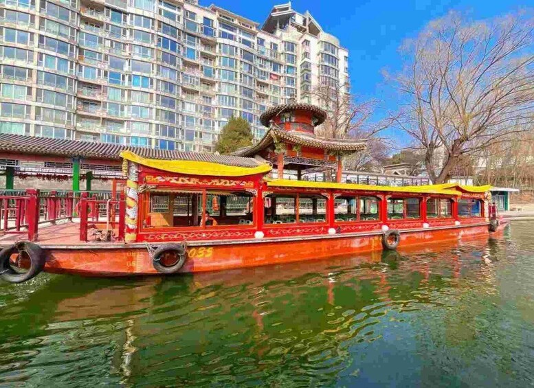 A traditional red boat with a yellow roof on a calm water body, with a modern building in the background. 5