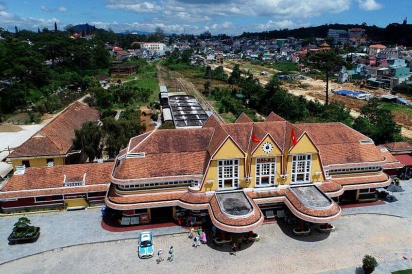 A large yellow building with a red roof, surrounded by greenery and a paved area with a car and people. 5