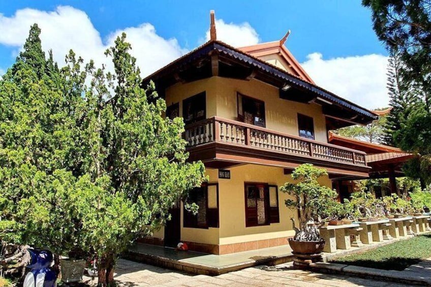 A traditional two-story building with a balcony, surrounded by trees and a well-maintained garden. 3