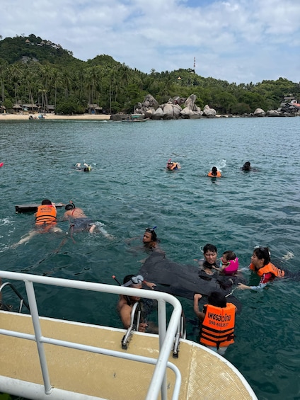 People swimming and snorkeling in a clear blue sea with a boat in the foreground. 5
