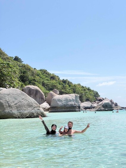 A beach with clear turquoise water, large boulders, and lush greenery. 4