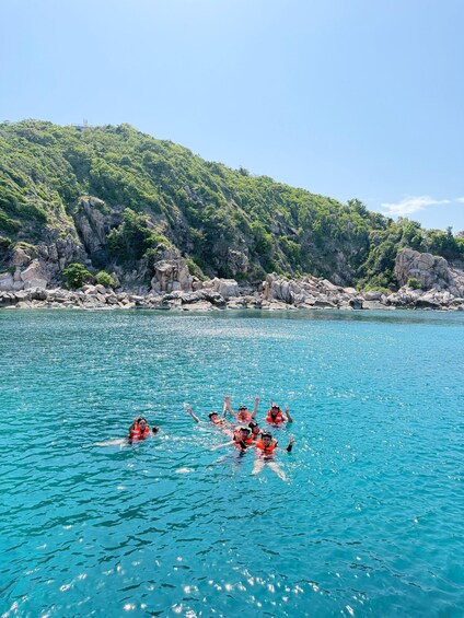 A group of people swimming in a clear blue sea with rocky cliffs in the background. 5
