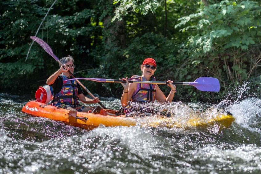 Two people kayaking on a river surrounded by greenery. 1
