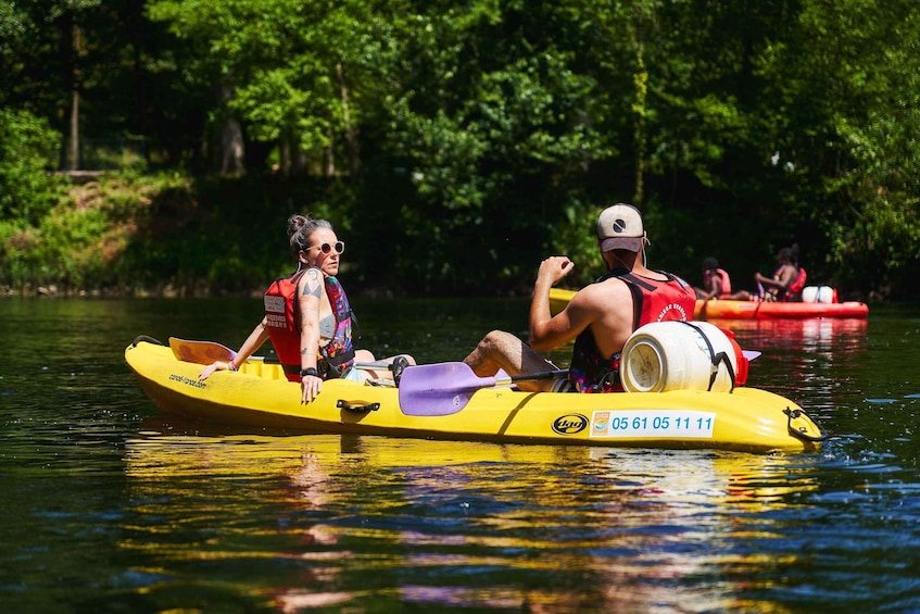 Two people kayaking on a yellow raft with a paddle and life jacket, surrounded by a calm river and greenery. 3