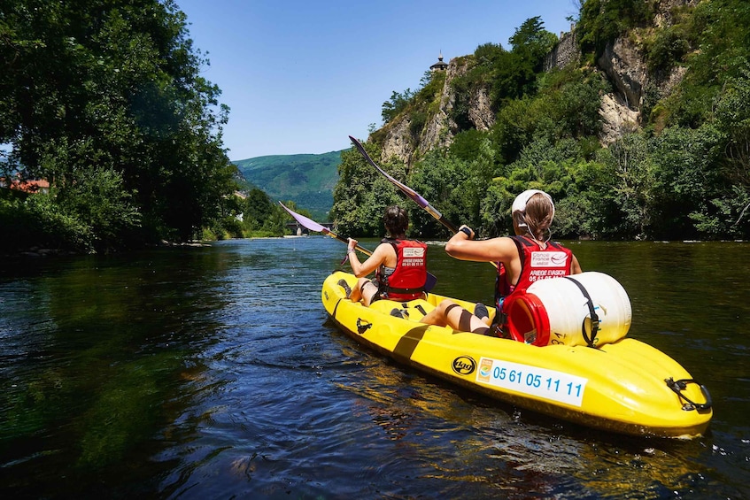 Two people kayaking on a yellow raft with a river and cliffs in the background. 2